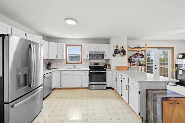 kitchen featuring white cabinets, appliances with stainless steel finishes, a sink, light countertops, and a peninsula