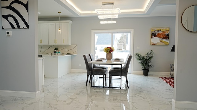 dining space featuring a raised ceiling, baseboards, marble finish floor, and a chandelier