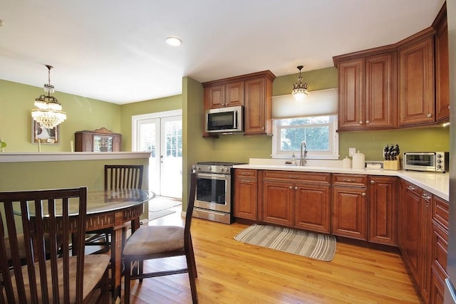 kitchen featuring light countertops, light wood-style flooring, appliances with stainless steel finishes, and pendant lighting