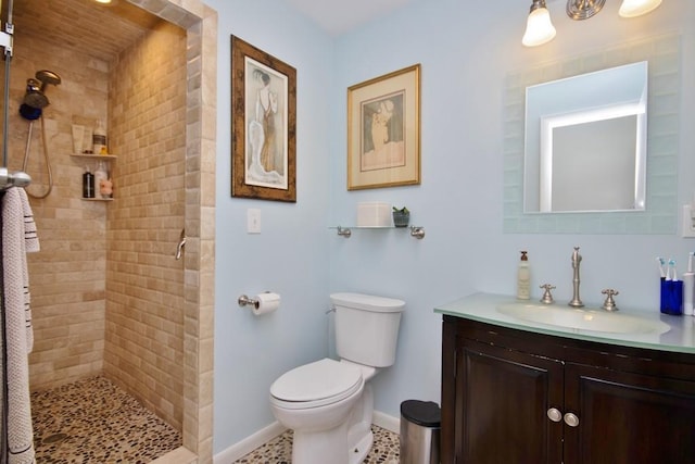 bathroom with baseboards, toilet, vanity, and a tile shower