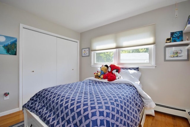 bedroom with a baseboard heating unit, wood finished floors, a closet, and baseboards