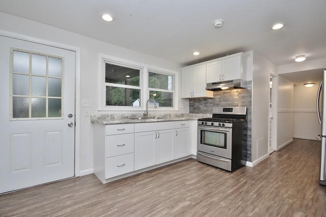 kitchen featuring stainless steel gas range oven, tasteful backsplash, under cabinet range hood, light wood-style floors, and a sink