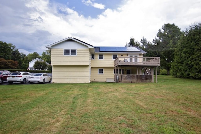 back of house featuring a deck, a lawn, and roof mounted solar panels