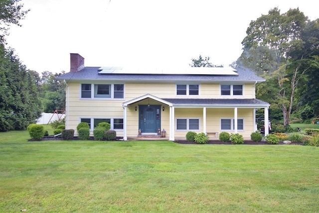 bi-level home with roof mounted solar panels, a chimney, and a front yard