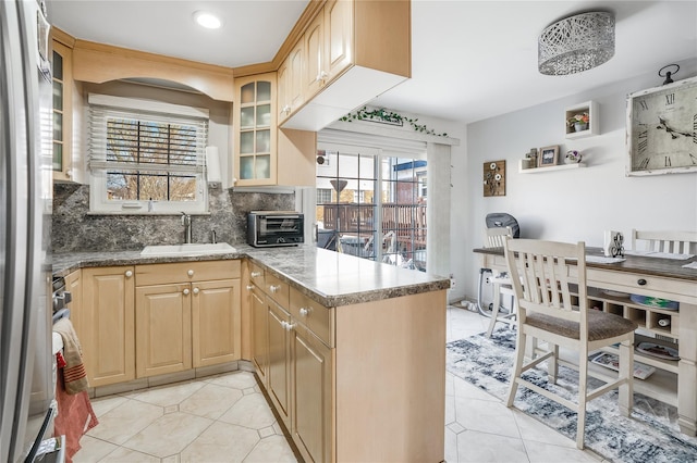 kitchen featuring stainless steel fridge, a peninsula, light brown cabinets, a sink, and backsplash