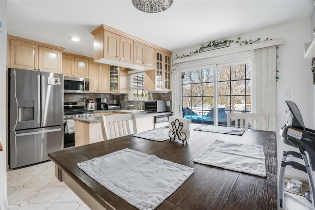 kitchen featuring tasteful backsplash, appliances with stainless steel finishes, glass insert cabinets, light brown cabinets, and a toaster