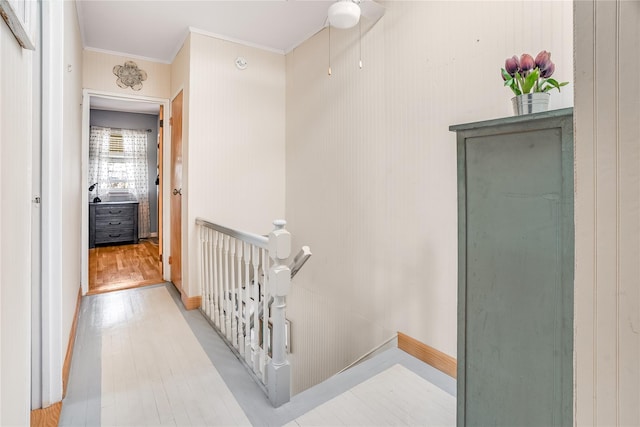 hallway featuring baseboards, an upstairs landing, wood finished floors, and ornamental molding