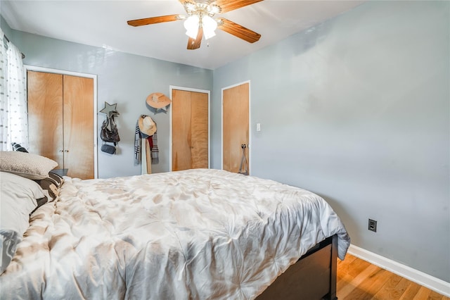 bedroom with baseboards, multiple closets, wood finished floors, and ceiling fan