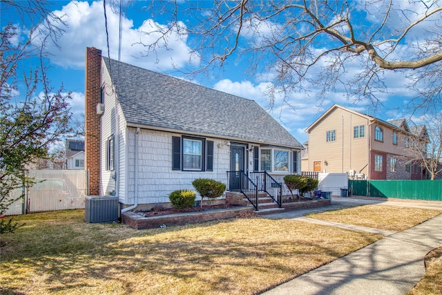 view of front of property with central air condition unit, fence, roof with shingles, a front yard, and a chimney