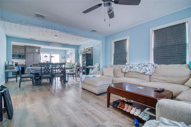 living room with a ceiling fan, visible vents, and light wood-type flooring