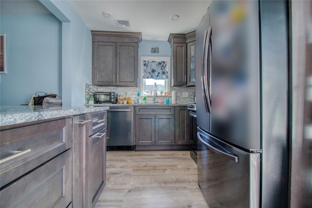 kitchen featuring visible vents, light wood-style flooring, a sink, tasteful backsplash, and stainless steel appliances