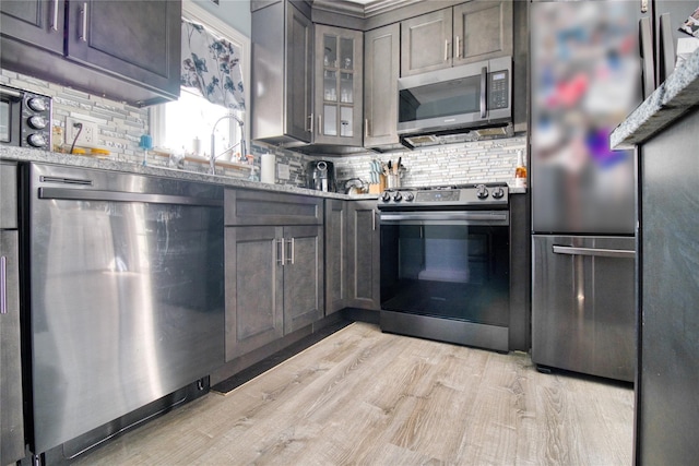 kitchen featuring gray cabinetry, glass insert cabinets, appliances with stainless steel finishes, light wood-type flooring, and backsplash