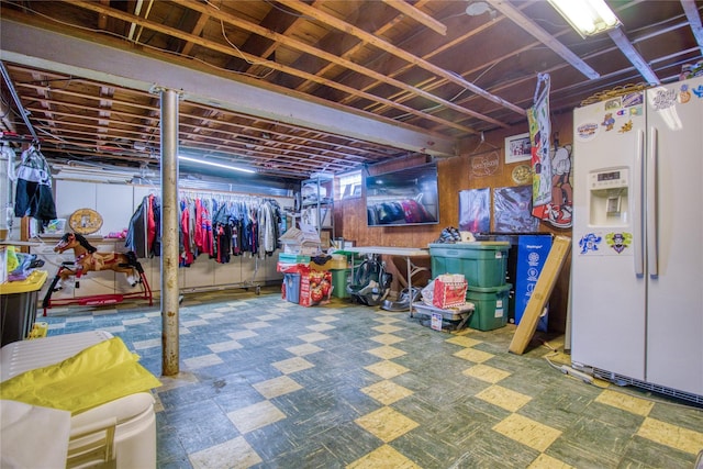 below grade area featuring tile patterned floors and white fridge with ice dispenser