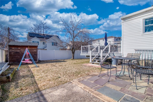 view of yard with a wooden deck, outdoor dining area, a fenced backyard, an outdoor structure, and a patio