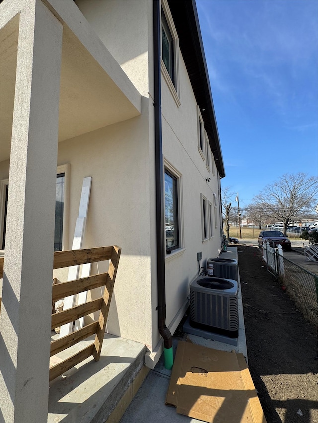 view of home's exterior with stucco siding, cooling unit, and fence