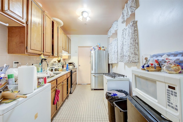 kitchen featuring under cabinet range hood, a sink, tasteful backsplash, appliances with stainless steel finishes, and light countertops