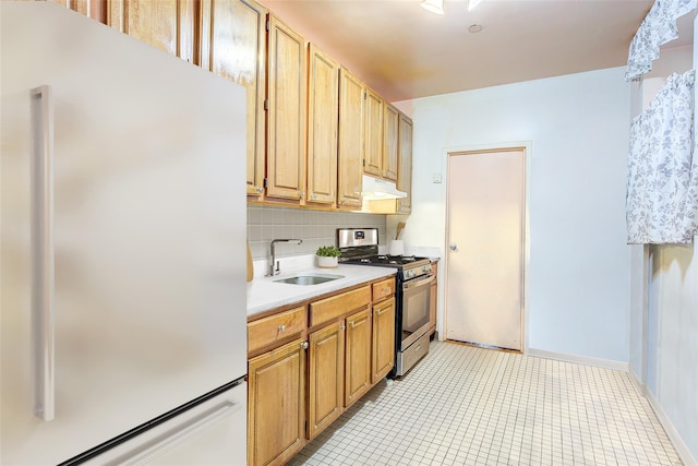 kitchen featuring stainless steel gas range, freestanding refrigerator, a sink, light countertops, and under cabinet range hood