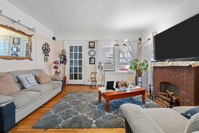 living area with cooling unit, wood finished floors, and a brick fireplace