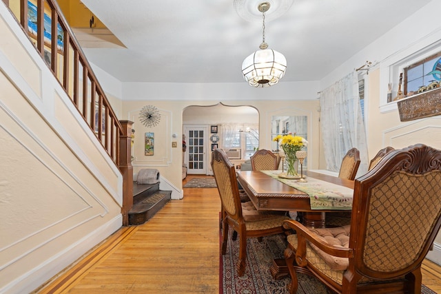 dining space with baseboards, arched walkways, an inviting chandelier, light wood-type flooring, and stairway