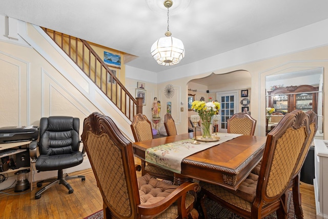 dining space with arched walkways, an inviting chandelier, hardwood / wood-style flooring, and stairs
