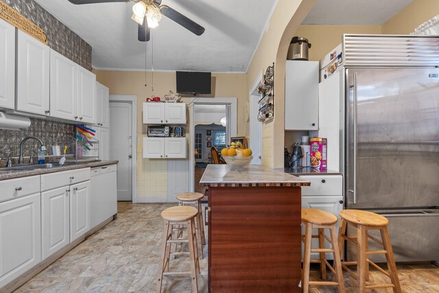 kitchen featuring built in fridge, white cabinets, ceiling fan, dishwasher, and a sink