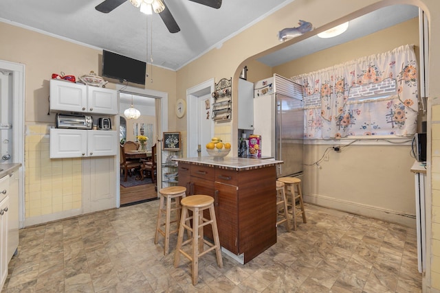 kitchen featuring stainless steel built in fridge, ornamental molding, white cabinetry, and arched walkways