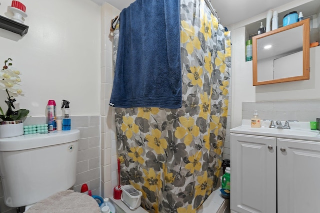 full bathroom with curtained shower, toilet, tile walls, vanity, and a wainscoted wall
