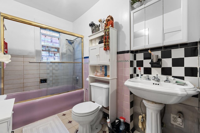 full bath featuring bath / shower combo with glass door, toilet, tile walls, a wainscoted wall, and tile patterned floors