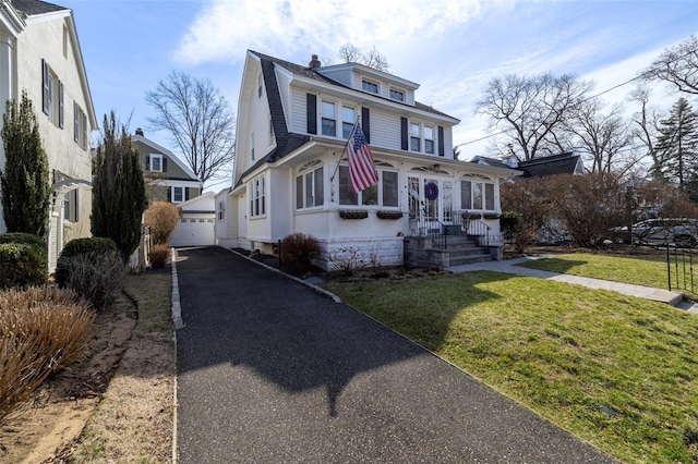 american foursquare style home featuring a detached garage, a front lawn, a gambrel roof, a chimney, and an outdoor structure