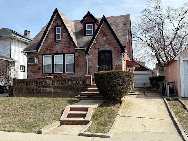 tudor house featuring brick siding, fence, an AC wall unit, a front yard, and an outdoor structure