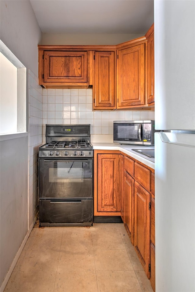 kitchen with stainless steel microwave, backsplash, freestanding refrigerator, brown cabinetry, and black range with gas cooktop