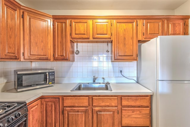 kitchen featuring stainless steel microwave, light countertops, decorative backsplash, freestanding refrigerator, and a sink