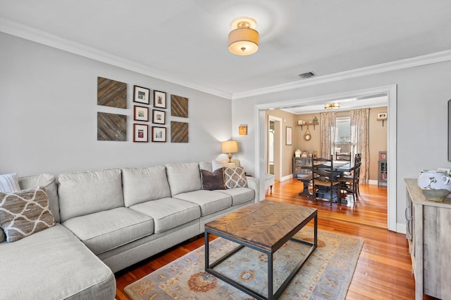 living area with visible vents, baseboards, ornamental molding, and light wood finished floors