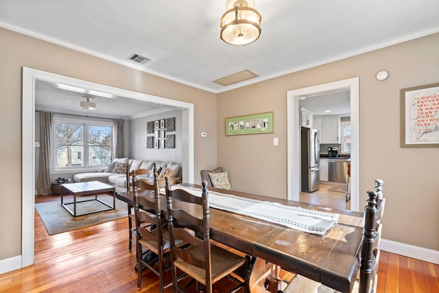 dining space featuring crown molding, light wood-style floors, visible vents, and baseboards