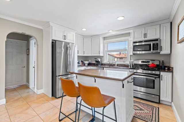 kitchen featuring butcher block countertops, light tile patterned floors, stainless steel appliances, arched walkways, and white cabinetry