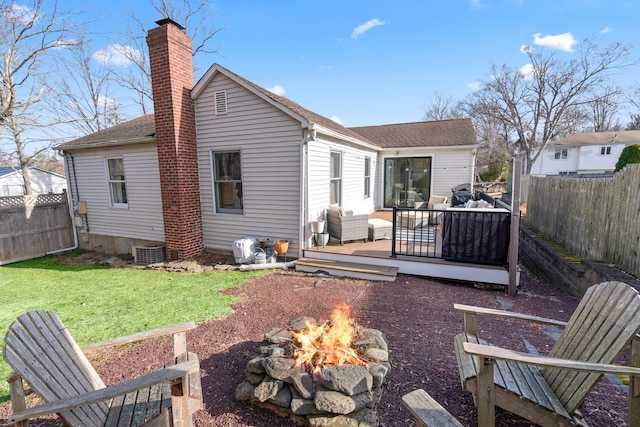 rear view of property featuring a wooden deck, an outdoor fire pit, a lawn, a chimney, and a fenced backyard