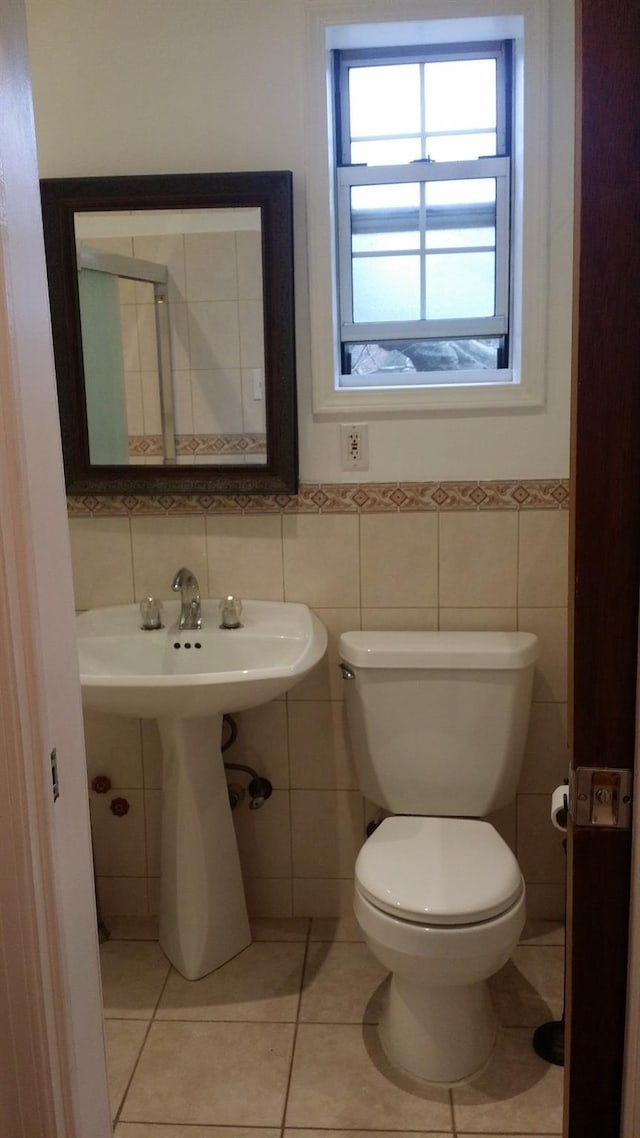 half bathroom with tile patterned floors, toilet, tile walls, and a wainscoted wall