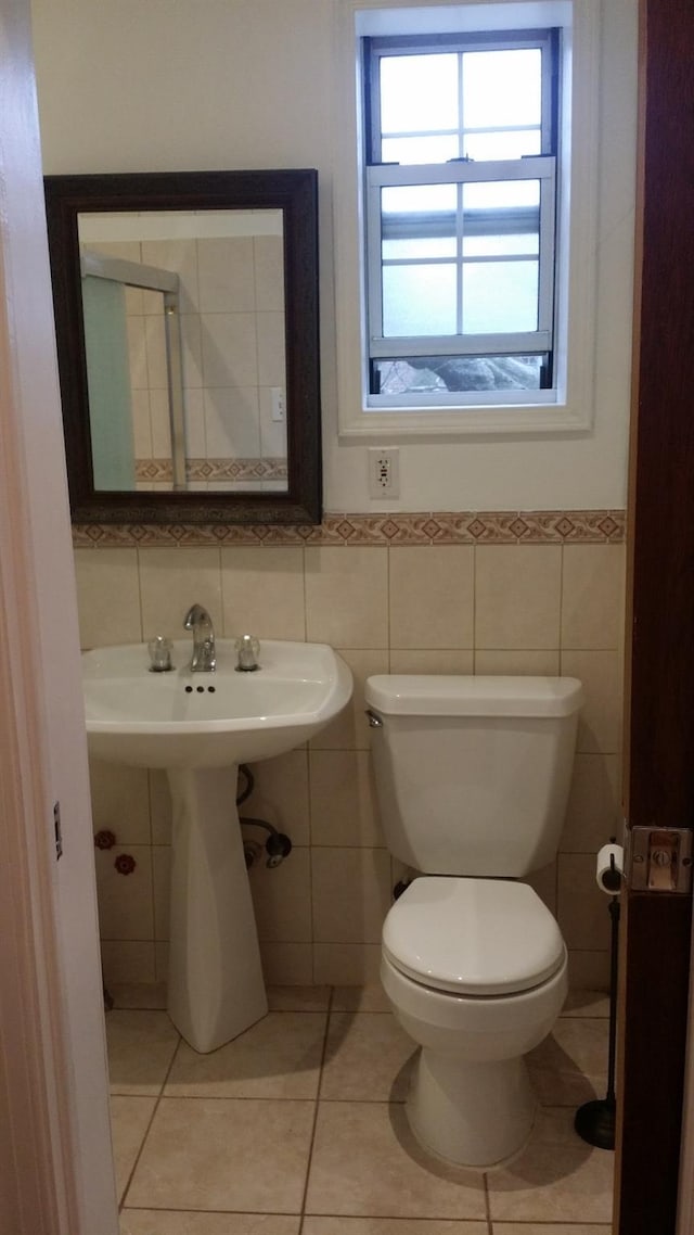 half bath featuring tile patterned flooring, tile walls, toilet, and a wainscoted wall