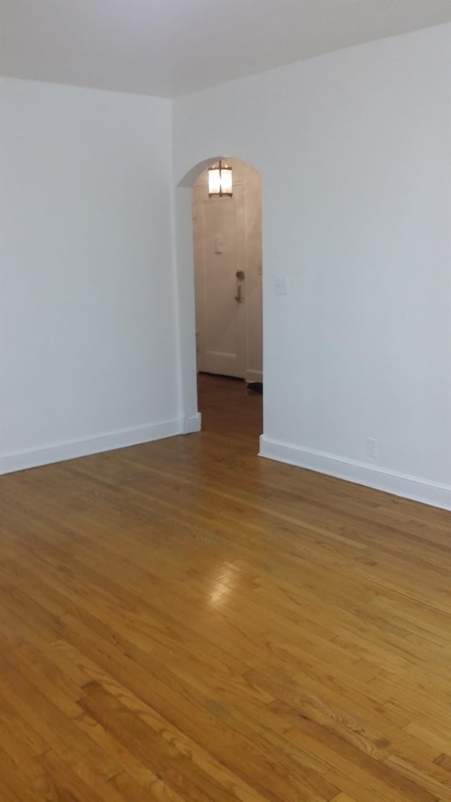 empty room featuring arched walkways, light wood finished floors, and baseboards