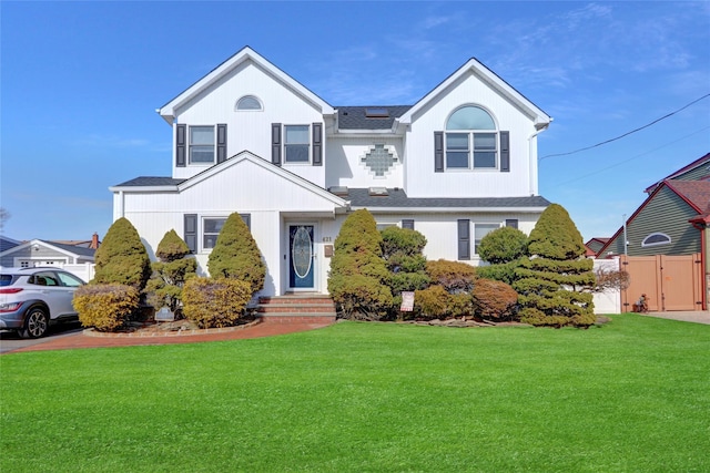 view of front facade with fence, roof with shingles, a front lawn, and a gate