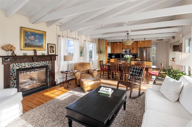 living room with a baseboard heating unit, a tiled fireplace, light wood-style flooring, and vaulted ceiling with beams