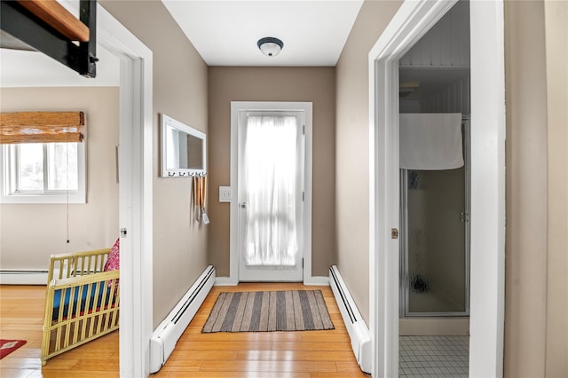 doorway with light wood finished floors, baseboard heating, and plenty of natural light