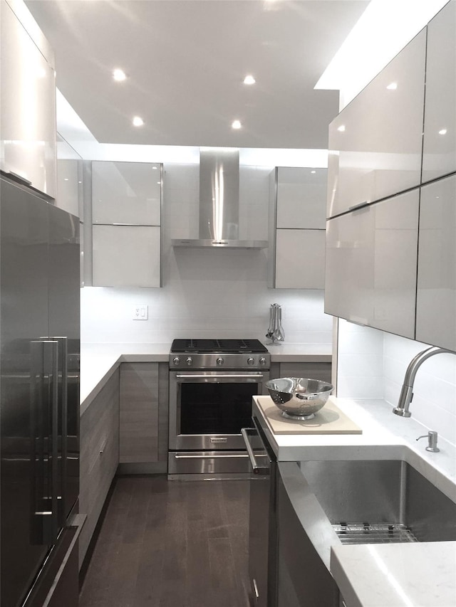 kitchen with stainless steel range with gas stovetop, light countertops, black refrigerator, wall chimney range hood, and modern cabinets