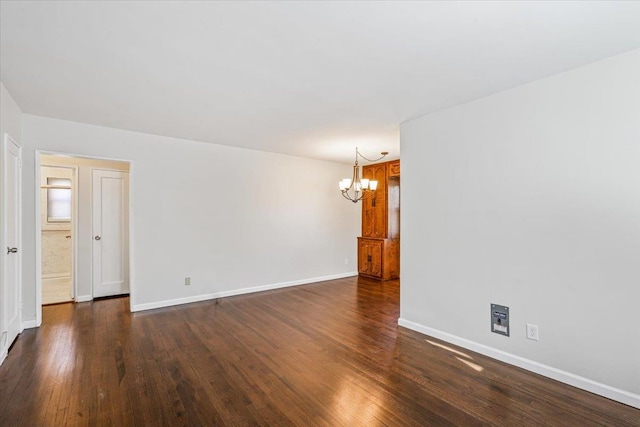 spare room with dark wood-type flooring, a notable chandelier, and baseboards