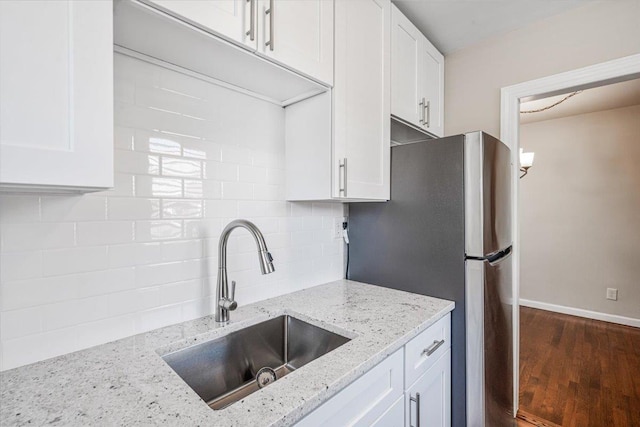 kitchen featuring light stone counters, white cabinets, freestanding refrigerator, and a sink