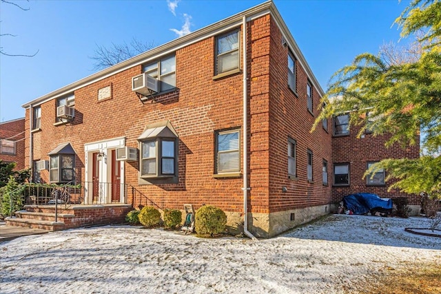 view of front of property with an AC wall unit, cooling unit, brick siding, and crawl space