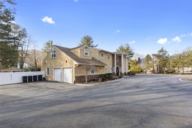 view of property exterior featuring stucco siding, aphalt driveway, stone siding, fence, and a garage