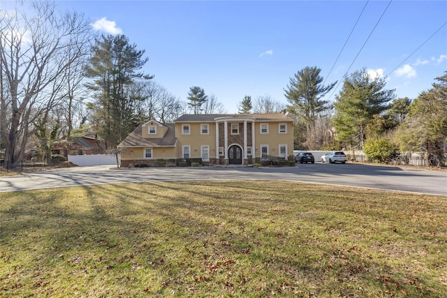 neoclassical / greek revival house with stucco siding, a front lawn, and fence