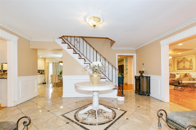 foyer entrance featuring stairway, a wainscoted wall, crown molding, and a decorative wall