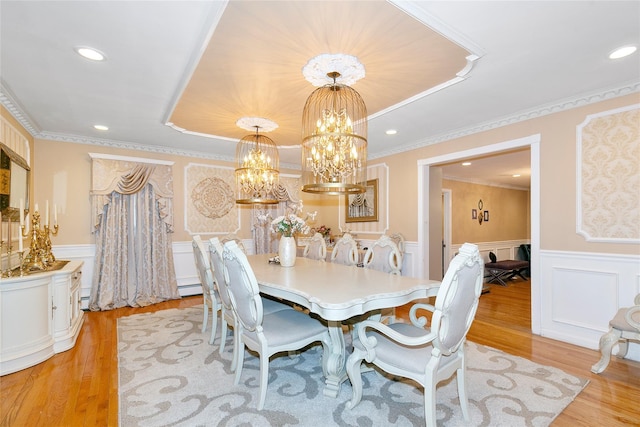 dining room featuring ornamental molding, light wood-style floors, an inviting chandelier, wainscoting, and a raised ceiling